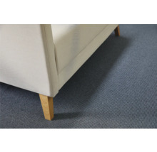 Detailansicht eines Polstermöbels mit Stoffbezug und Holzfüßen auf einem Teppichboden.