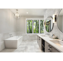 Helles Badezimmer mit Badewanne, Waschtisch und Fenster mit Blick in die Natur.