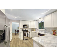 Helle Küche mit weißen Schränken, Edelstahlgeräten und Arbeitsplatten in Marmoroptik.