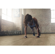 Frau macht Liegestütze auf einem Holzboden in einem Fitnessstudio.