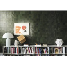 Wandgestaltung mit quadratischen Fliesen über einem Bücherregal mit Dekorationsgegenständen.