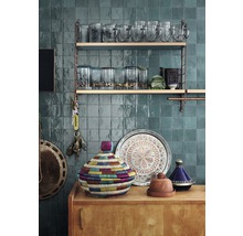 Dekorative Gegenstände auf einem Holzschrank vor einer gefliesten Wand und Regalen mit Gläsern