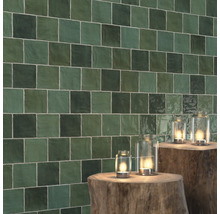 Wand mit quadratischen, grünen Fliesen und Windlichtern auf Baumstümpfen