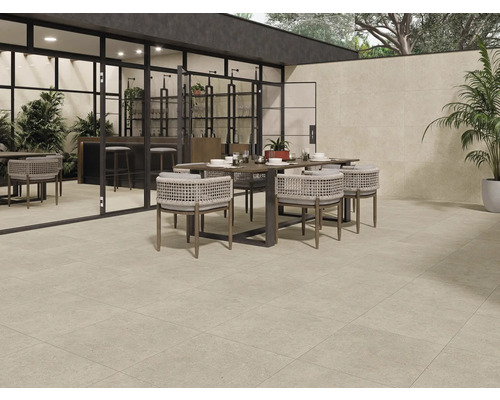 Terrasse mit Bodenfliesen, Esstisch und Stühlen vor einem Haus mit großen Fenstern.