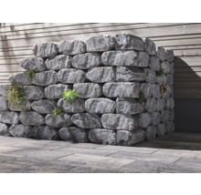 Gestapelte graue Pflanzsteine mit Bepflanzung vor einer Holzwand