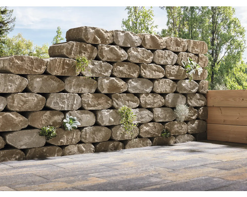 Eine Trockenmauer aus Natursteinen mit Bepflanzung im Garten.