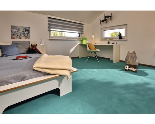 Helles Jugendzimmer mit Bett, Schreibtisch und türkisfarbenem Teppichboden.