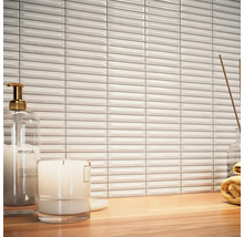 Szene mit weißen, länglichen Wandfliesen, Seifenspender, Kerze und Handtuch auf einem Holztisch