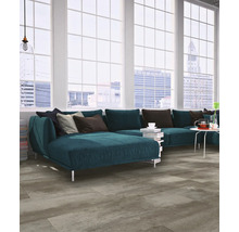 Modernes Wohnzimmer mit grauem Boden in Betonoptik, blauem Ecksofa und großen Sprossenfenstern mit Stadtblick.