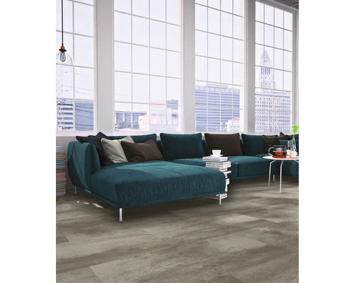 Modernes Wohnzimmer mit grauem Boden in Betonoptik, blauem Ecksofa und großen Sprossenfenstern mit Stadtblick.