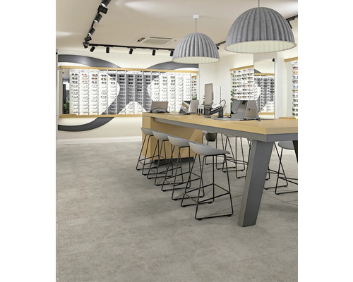 Moderne Raumgestaltung mit großformatigen grauen Bodenfliesen in Steinoptik, einem hohen Holztisch mit Barhockern und großen Pendelleuchten.