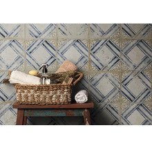 Dekorative Fliesenwand mit geometrischem Muster und Korb mit Badezimmerartikeln auf einem Hocker