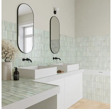 Helles Badezimmer mit zwei weißen Aufsatzwaschbecken, ovalen Spiegeln, schwarzen Armaturen und hellgrünen vertikalen Wandfliesen.