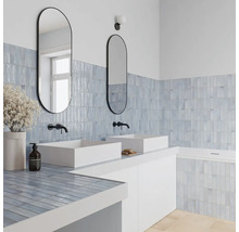 Modernes Badezimmer mit zwei weißen Aufsatzwaschbecken, schwarzen Wandarmaturen und ovalen Spiegeln. Hellblaue Fliesen an Wand und Badewanne.