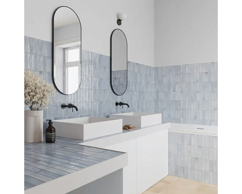 Modernes Badezimmer mit zwei weißen Aufsatzwaschbecken, schwarzen Wandarmaturen und ovalen Spiegeln. Hellblaue Fliesen an Wand und Badewanne.