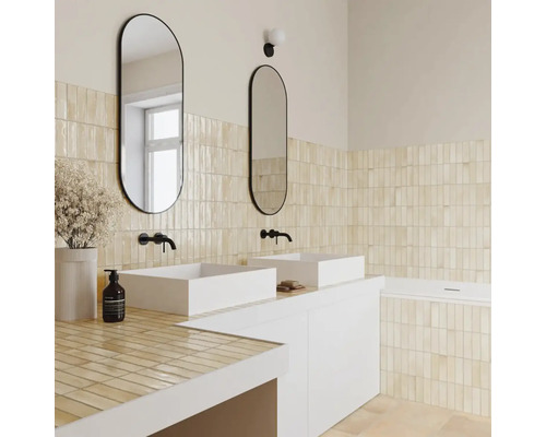 Helles Badezimmer mit beigen vertikalen Wandfliesen, weißen Aufsatzwaschbecken, schwarzen Wandarmaturen und ovalen Spiegeln.