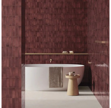 Modernes Badezimmer mit vertikal verlegten, dunkelroten Wandfliesen, einer freistehenden weißen Badewanne und einem Beistelltisch aus Holz.