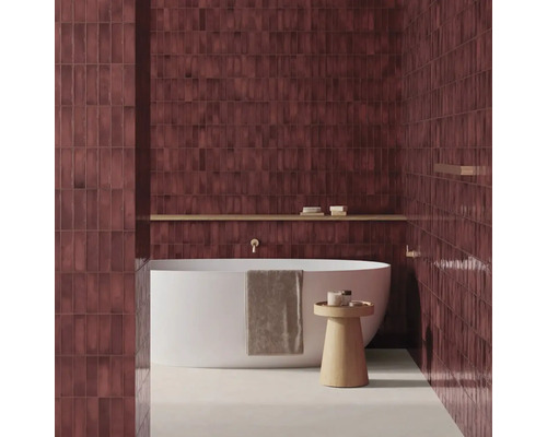 Modernes Badezimmer mit vertikal verlegten, dunkelroten Wandfliesen, einer freistehenden weißen Badewanne und einem Beistelltisch aus Holz.
