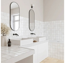 Modernes Badezimmer mit zwei weißen Aufsatzwaschbecken, schwarzen Wandarmaturen, ovalen Spiegeln und quadratischen weißen Fliesen.