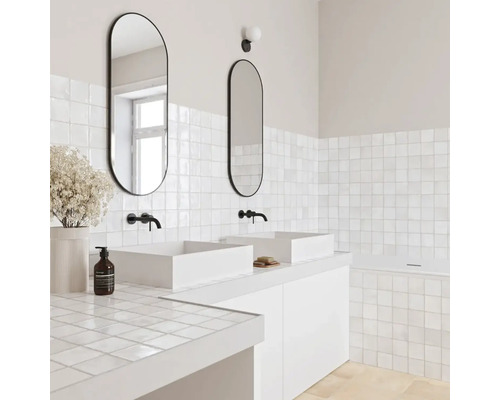 Modernes Badezimmer mit zwei weißen Aufsatzwaschbecken, schwarzen Wandarmaturen, ovalen Spiegeln und quadratischen weißen Fliesen.