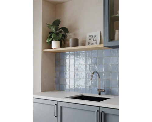 Moderne Küche mit blauem Fliesenspiegel, glänzenden quadratischen Wandfliesen, hellem Holzregal, Chrom-Armatur und schwarzem Einbaubecken.