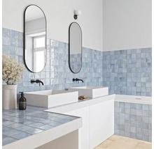 Modernes Badezimmer mit hellblauen quadratischen Wandfliesen, zwei weißen Aufsatzwaschbecken, schwarzen Armaturen und ovalen Spiegeln.