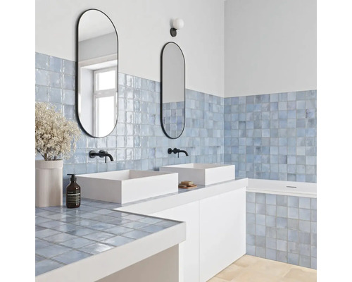 Modernes Badezimmer mit hellblauen quadratischen Wandfliesen, zwei weißen Aufsatzwaschbecken, schwarzen Armaturen und ovalen Spiegeln.
