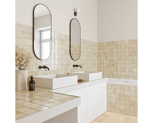 Helles Badezimmer mit zwei weißen Aufsatzwaschbecken, schwarzen Wandarmaturen, ovalen Spiegeln und beigen quadratischen Wandfliesen.