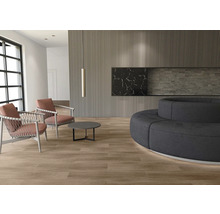 Moderner Wohnraum mit hellem Boden in Holzoptik, Wandverkleidung aus Holzlamellen, zwei Sesseln, einem runden Tisch und einem großen Rundsofa.