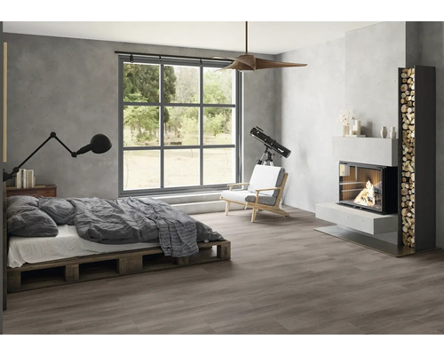 Modernes Schlafzimmer im Industrial Style mit dunklem Boden in Holzoptik, grauen Wänden in Betonoptik, Palettenbett, großem Fenster und Kamin.