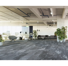Moderner, heller Büroraum mit dunkelgrauem Bodenbelag in Steinoptik, Glaswänden, grauem Sofa, Pflanzen und industrieller Decke.