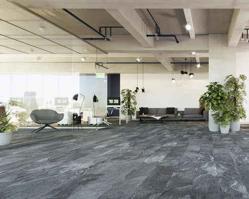Moderner, heller Büroraum mit dunkelgrauem Bodenbelag in Steinoptik, Glaswänden, grauem Sofa, Pflanzen und industrieller Decke.