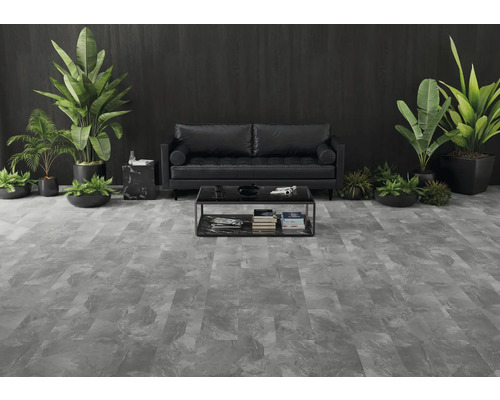 Modernes Wohnzimmer mit grauem Bodenbelag in Steinoptik, schwarzem Ledersofa, dunkler Holzwand und großen Zimmerpflanzen.