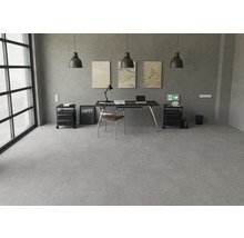 Moderner Arbeitsbereich mit grauem Bodenbelag in Betonoptik, schwarzem Schreibtisch und industriellen Pendelleuchten vor einer Betonwand.