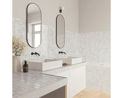 Modernes helles Badezimmer mit weißen Mosaikfliesen an Wänden und Waschtisch, zwei weißen Aufsatzbecken, schwarzen Armaturen und ovalen Spiegeln.