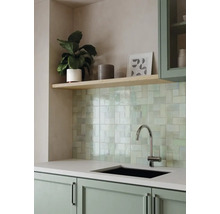 Moderne Küche mit hellgrün glänzenden Wandfliesen, schwarzer Spüle, verchromtem Wasserhahn und salbeigrünen Küchenschränken.