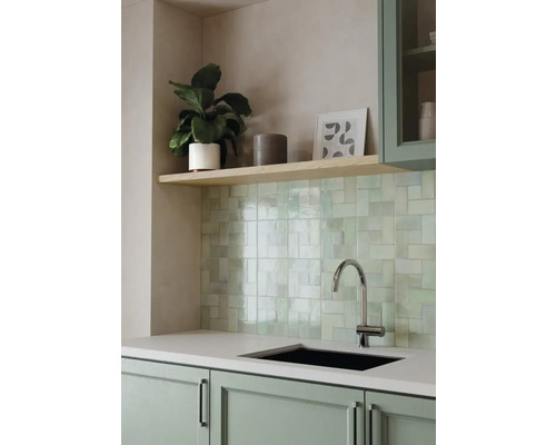 Moderne Küche mit hellgrün glänzenden Wandfliesen, schwarzer Spüle, verchromtem Wasserhahn und salbeigrünen Küchenschränken.