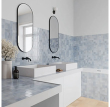 Modernes Badezimmer mit zwei weißen Aufsatzwaschbecken, schwarzen Wandarmaturen, zwei ovalen Spiegeln und blauen quadratischen Wandfliesen.