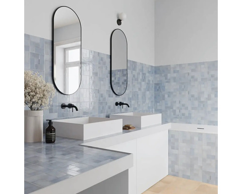 Modernes Badezimmer mit zwei weißen Aufsatzwaschbecken, schwarzen Wandarmaturen, zwei ovalen Spiegeln und blauen quadratischen Wandfliesen.