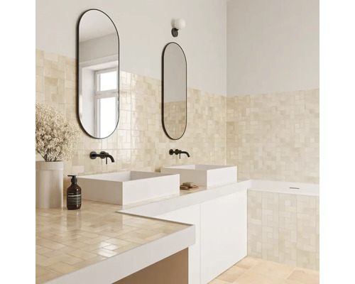 Modernes Badezimmer mit beigen Wandfliesen, zwei weißen Aufsatzwaschbecken, ovalen Spiegeln mit schwarzem Rahmen und schwarzen Wandarmaturen.