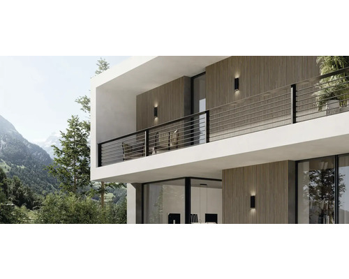 Modernes Haus mit Außenwandleuchten und Balkon vor Bergkulisse.