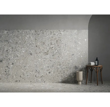 Modern gestalteter Raum mit Wand- und Bodenfliesen in Terrazzo-Optik, einem runden Beistelltisch aus Holz und einer Bodenvase.