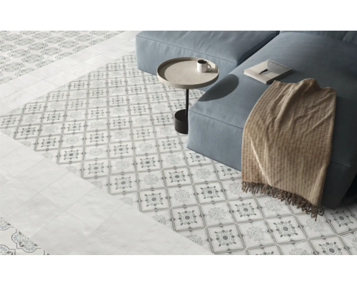 Hell gestalteter Wohnbereich mit dekorativ gemusterten Bodenfliesen, schlichten Fliesen im Randbereich und einem Sofa.