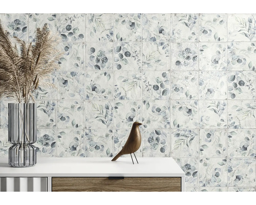 Wandfliesen mit botanischem Blattmuster in einer hellen Raumsituation mit Glasvase und Holzfigur auf einer Kommode.