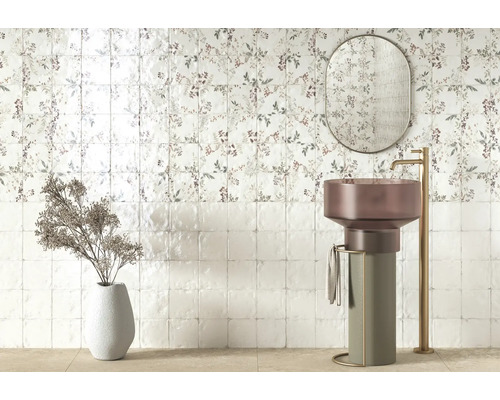 Modernes Badezimmer mit floralen Wandfliesen, freistehendem Säulenwaschbecken, hoher goldfarbener Armatur, ovalem Spiegel und Dekovase.