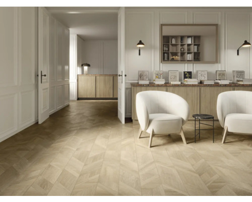 Heller Wohnraum mit Parkettboden im Fischgrätmuster, zwei weißen Sesseln, Sideboard aus Holz und wandmontierten Lampen.
