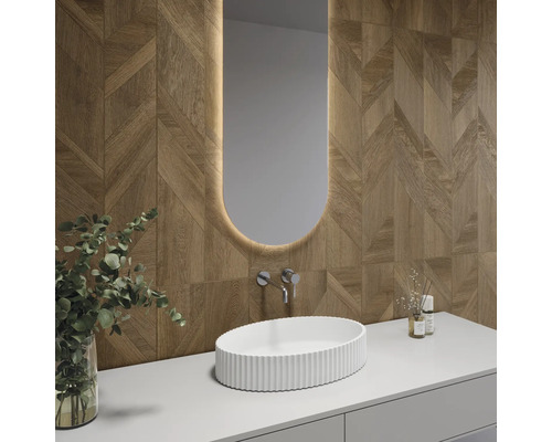 Modernes Badezimmer mit Wandfliesen in Holzoptik und geometrischem Muster, weißem Aufsatzwaschbecken und beleuchtetem ovalem Spiegel.