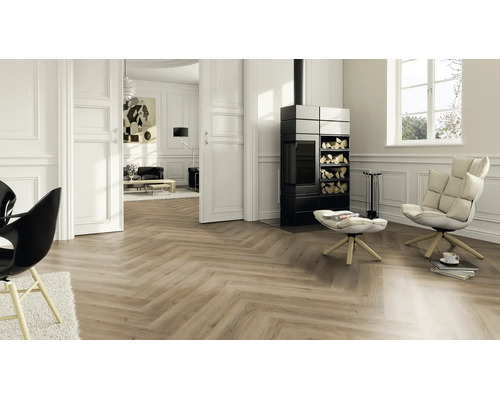 Helles Wohnzimmer mit Laminatboden in Fischgrät-Optik, schwarzem Kaminofen, weißem Sessel und Wandpaneelen.