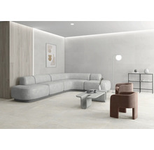 Heller, moderner Wohnraum mit großformatigen Fliesen an Wand und Boden, geschwungenem Ecksofa, Betontisch und minimalistischer Einrichtung.