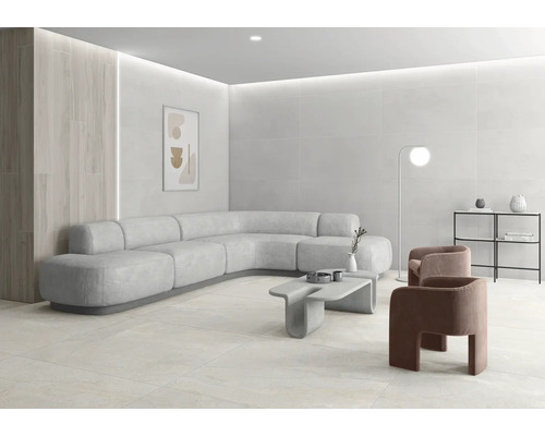 Heller, moderner Wohnraum mit großformatigen Fliesen an Wand und Boden, geschwungenem Ecksofa, Betontisch und minimalistischer Einrichtung.